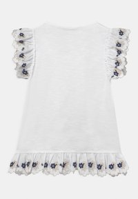 Biała koszula z krótkim rękawem z falbanami, zdobiona haftem kwiatowym w odcieniach granatu i złota. Ząbkowane wykończenie z podobnymi akcentami kwiatowymi na dole.