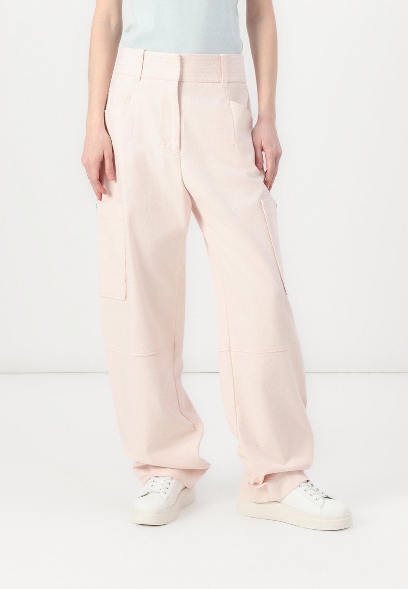 Pantalons cargo larges rose clair en coton doux. Comprend des poches latérales, une taille haute, et une coupe décontractée. Associés à des baskets blanches.