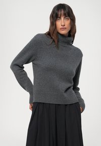 Grå turtleneck genser, laget av mykt strikket stoff, har ribbestrikket kant og mansjetter, med en avslappet passform, kombinert med et svart skjørt.