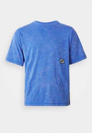 Blå kortærmet T-shirt lavet af blødt stof, med en falmet tekstur og et lille sort-hvidt logo-patch på venstre bryst.