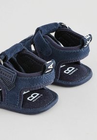Sandales pour bébé en tissu doux bleu marine avec brides réglables et étiquettes de marque, adaptées aux nourrissons de 0 à 3 mois.