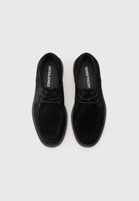 Schwarze Wildlederschuhe mit runder Zehenpartie, die über ein einfaches Schnürdesign, kontrastierende Nähte und eine strukturierte Gummisohle verfügen.