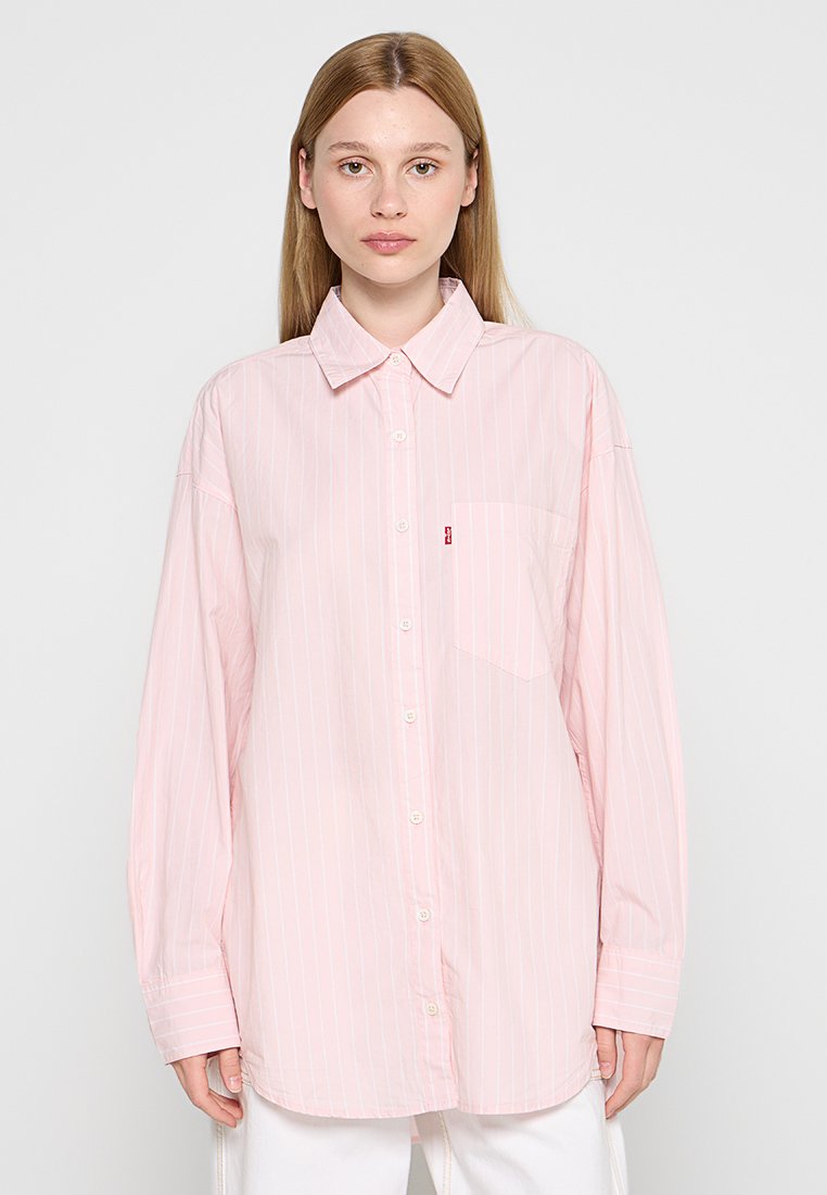 Chemise rayée rose clair avec un devant à boutons, un col pointu, des manches longues et une poche poitrine avec un petit logo. Texture du tissu lisse.