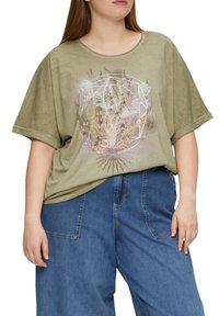 Oliwkowa, oversize koszulka z okrągłym dekoltem i krótkimi rękawami; ma kwiatowy wzór geometryczny w kolorach różowym, białym i żółtym.