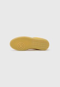 Gelbe Sneakersohle mit einer strukturierten Gummifläche, die eine runde Vertiefung und rautenförmige Muster für die Traktion aufweist.