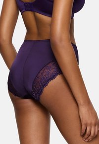 Hlačne visoko pasu v vijolični barvi, izdelane iz neprosojnega materiala in s prosojnim čipkastim okrasom. Imajo cvetlične motive vzdolž robov in valovit zaključek.