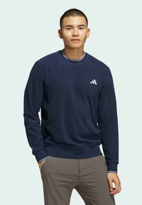 Felpa blu navy realizzata in tessuto morbido, con maniche lunghe, polsini e orlo a coste, e logo Adidas sul petto a sinistra.