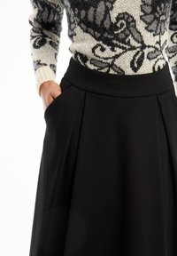 Zwarte plissé rok met een gestructureerde tailleband, ontworpen met zakken. De stof lijkt glad met een matte afwerking.