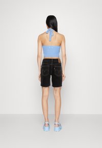 Světle modrý háčkovaný halter top, černé džíny s potrhanými okraji a světle modré platformové sandály. Pohled ze zad.