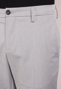 Gray and white textured trousers with a button closure, featuring a woven pattern and side pockets, made from a lightweight fabric.