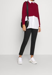 Punainen neule cropped-paita valkoisen kauluspaidan päällä, yhdistettynä mustiin kapeisiin housuihin ja valkoisiin urheilulenkkareihin. Yksinkertainen musta olkalaukku.