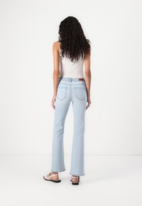 Jeans flare de culoare albastru deschis cu talie înaltă, având un design standard cu cinci buzunare și un eticheta din piele maro pe talie.