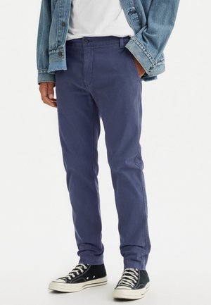 Chinos en coton marine avec une coupe slim, poches avant et fermeture par bouton, associés à des baskets montantes noires et une veste en jean.
