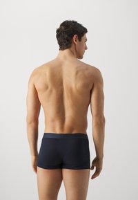 Boxer-briefs bleu marine foncé en tissu lisse et extensible, dotés d'une large ceinture. Modèle vu de dos, montrant une silhouette musclée.