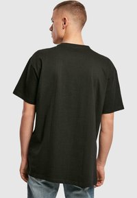 Black cotton t-shirt with a relaxed fit, short sleeves, a crew neckline, and a straight hem. Back view shows a smooth texture and simple design.
