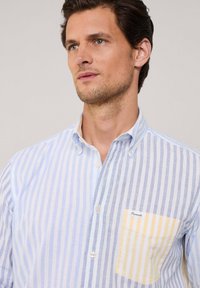 Camisa de manga corta abotonada en rayas azul claro y blancas, con un bolsillo a rayas amarillas y fabricada en suave material de algodón.