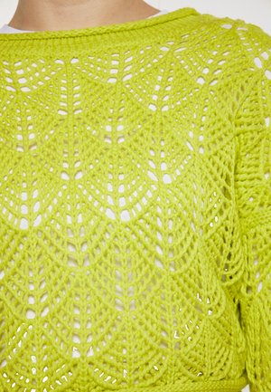 Limettengrüner Strickpullover mit offenem Maschenmuster, featuring einem geometrischen Design und weicher Textur. Lichtakzente durch den Stoff.