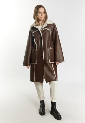 Cappotto in pelle marrone con collo in shearling, cuciture bianche a contrasto e due grandi tasche frontali. Presenta una vestibilità ampia e oversize.
