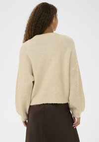 Maglione beige con maniche ampie, caratterizzato da dettagli testurizzati e piccole perle lungo le maniche. Materiale morbido e leggero con design corto.