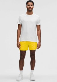 Vit kortärmad idrottströja med ribbad textur, i kombination med ljusgula shorts. Modellen bär vita sneakers och vita strumpor i ankellängd.