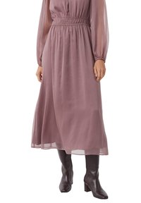 Długa, zwiewna sukienka w mauve z przejrzystymi, długimi rękawami, elastycznym stanikiem i długości midi. Noszona z gładkimi, ciemnobrązowymi botkami na obcasie.