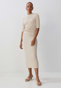 Beige gestricktes Zweiteiler-Outfit mit einem taillierten Midirock und einem kurzärmligen Oberteil, texturiertem Stoff und Rundhalsausschnitt. Beinhaltet Absatzsandalen.