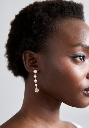 Ciondoli oro con tre perle bianche e un cristallo a goccia trasparente sul fondo, esposti su uno sfondo neutro.