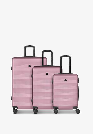 Conjunto de tres maletas rígidas rosas con asas negras y cuatro ruedas, dispuestas por tamaño de grande a pequeño sobre un fondo blanco.
