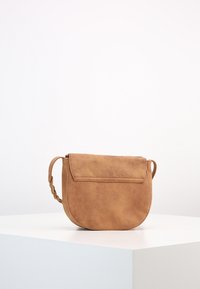 Brązowa torebka typu crossbody z futerkiem sztucznym o zakrzywionym kształcie, zamykana na klapkę oraz z plecionym paskiem. Gładka struktura z drobnymi oznakami na powierzchni.