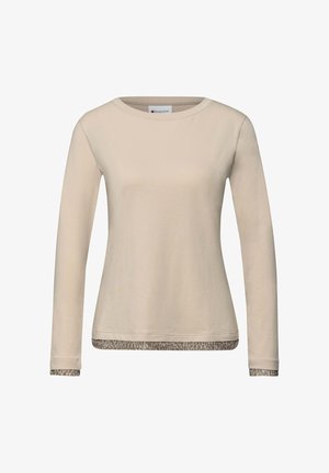 Pitkähihainen beige T-paita, joka on valmistettu pehmeästä kankaasta. Paidassa on kontrastinväriset eläinkuviolliset reunat helmassa ja hihansuissa. Pyöreä kaula-aukko, yksinkertainen linjakas muotoilu.