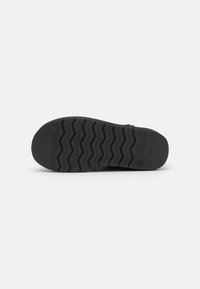 Sole di scarpa in gomma nera con un motivo a zigzag, caratterizzata da una superficie liscia e un profilo piatto, progettata per offrire trazione e durata.