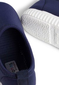 Zapatos de tela azul marino tipo slip-on con suelas de goma blanca. Presentan una textura suave y costuras sutiles, diseñados para brindar comodidad y facilidad de uso.