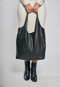 Czarna skórzana torba typu tote z miękkim, teksturowanym wykończeniem, wyposażona w szerokie paski na ramię i pojemny design. Bez widocznych elementów metalowych czy zdobień.