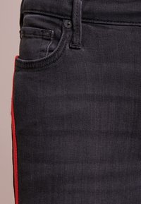 Svarta denimjeans med en röd sidslits, femfickdesign och subtil textur. Inkluderar en synlig knappstängning och bälteshällor.