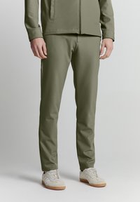 Olivengrüne, maßgeschneiderte Hose aus glattem Stoff. Mit schlanker Passform, seitlichen Taschen und kombiniert mit hellen Sneakers.