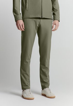 Olijfgroene, op maat gemaakte broeken van een zachte stof. Met een slim fit, zijzakken en gecombineerd met lichte sneakers.