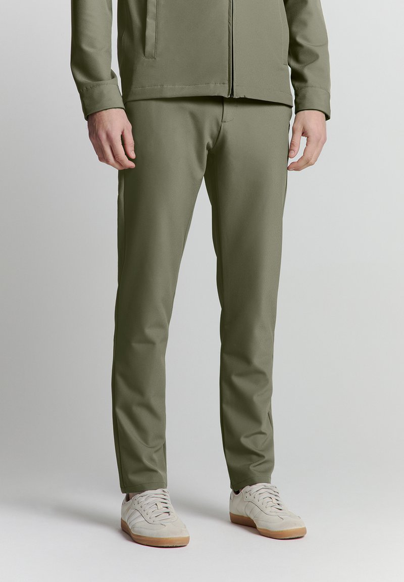 Olivengrüne, maßgeschneiderte Hose aus glattem Stoff. Mit schlanker Passform, seitlichen Taschen und kombiniert mit hellen Sneakers.