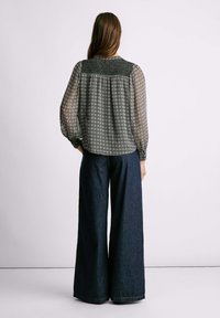 Blusa a maniche lunghe con un motivo geometrico bianco e nero, con giromanica arricciato, abbinata a pantaloni in denim scuri a gamba larga. Tessuto leggero e testurizzato.