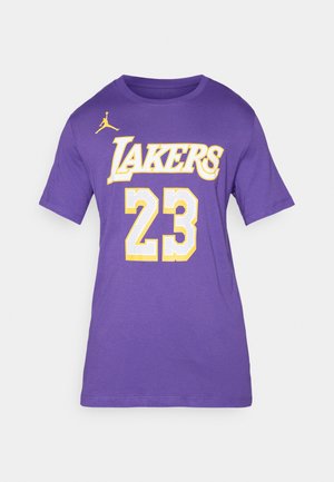 Camiseta corta de manga en color púrpura con "LAKERS" en amarillo sobre un número "23" perforado en blanco, que presenta un logo Jumpman amarillo en el hombro izquierdo.