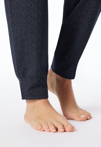 Navy legging met een gestructureerd geometrisch patroon, aansluitende enkels en een zachte stoffen afwerking. Blote voeten ernaast geplaatst.