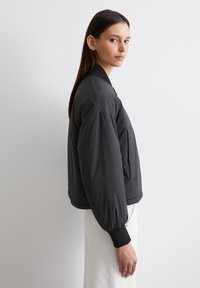 Schwarze Bomberjacke mit glatter Textur, gerippten Bündchen und Reißverschluss vorne. Verfügt über eine lockere Passform und seitliche Taschen.