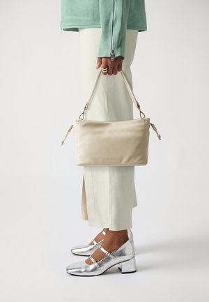 Borsa a tracolla in pelle beige con accenti intrecciati, portata da una persona in giacca verde menta e pantaloni color crema, abbinata a scarpe con tacco a blocco argentate.