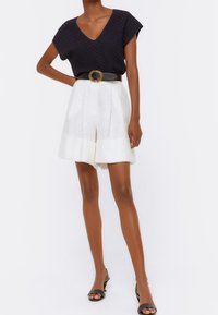 Marineblauw getextureerd kortmouwen shirt met V-hals, gecombineerd met witte plooien hoge taille shorts en een zwarte riem met een ronde gesp.