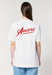 Balta kokvilnas T-kreklu ar izteiksmīgu sarkano "Amore" tekstu uz aizmugures. Īsas piedurknes, brīvs piegriezums un apaļa kakla izgriezums.