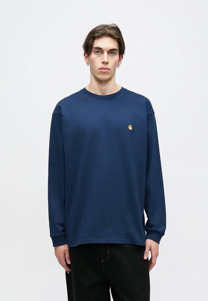 Marineblå langærmet T-shirt lavet af bomuld med rund hals. Har et lille gult logo på brystet. Modellen bærer sorte bukser.