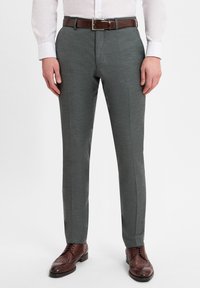 Dark grey tailored trousers with a smooth texture, featuring a slim fit, front creases, and a brown leather belt. Brown brogue shoes complete the look.