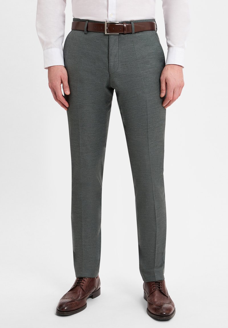 Dark grey tailored trousers with a smooth texture, featuring a slim fit, front creases, and a brown leather belt. Brown brogue shoes complete the look.