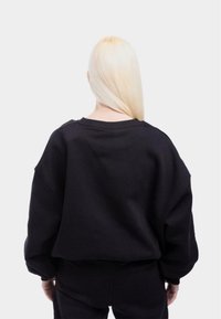 Felpa nera oversize con scollatura tonda, spalle abbassate e tessuto morbido, con una parte posteriore testurizzata e vestibilità rilassata.