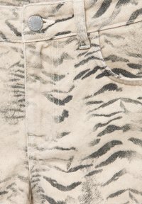 Gros plan d'un tissu en denim beige avec un motif de rayures de tigre noires et un bouton métallique sur la ceinture près de la poche avant.