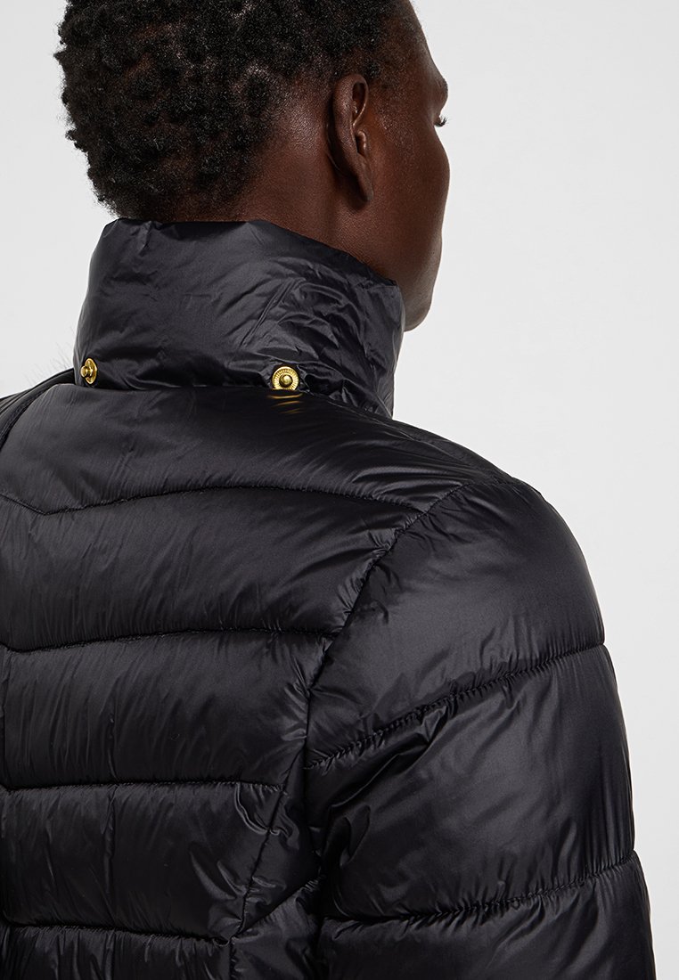Schwarze gepolsterte Jacke mit hohem Kragen, ausgestattet mit einer glänzenden Textur und goldfarbenen Druckknöpfen am Kragen. Zickzack-Nähte sind auf dem Stoff sichtbar.